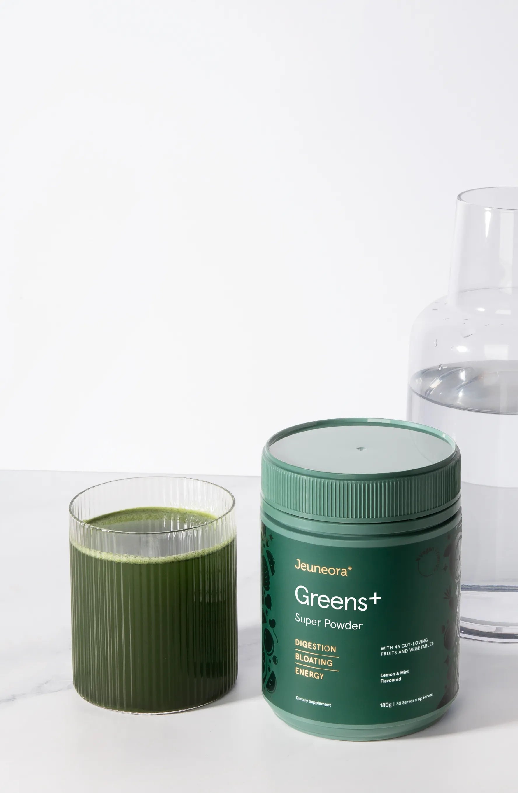 A container of Jeuneora Greens+ Super powder next to a glass of the supplement mixed into water.