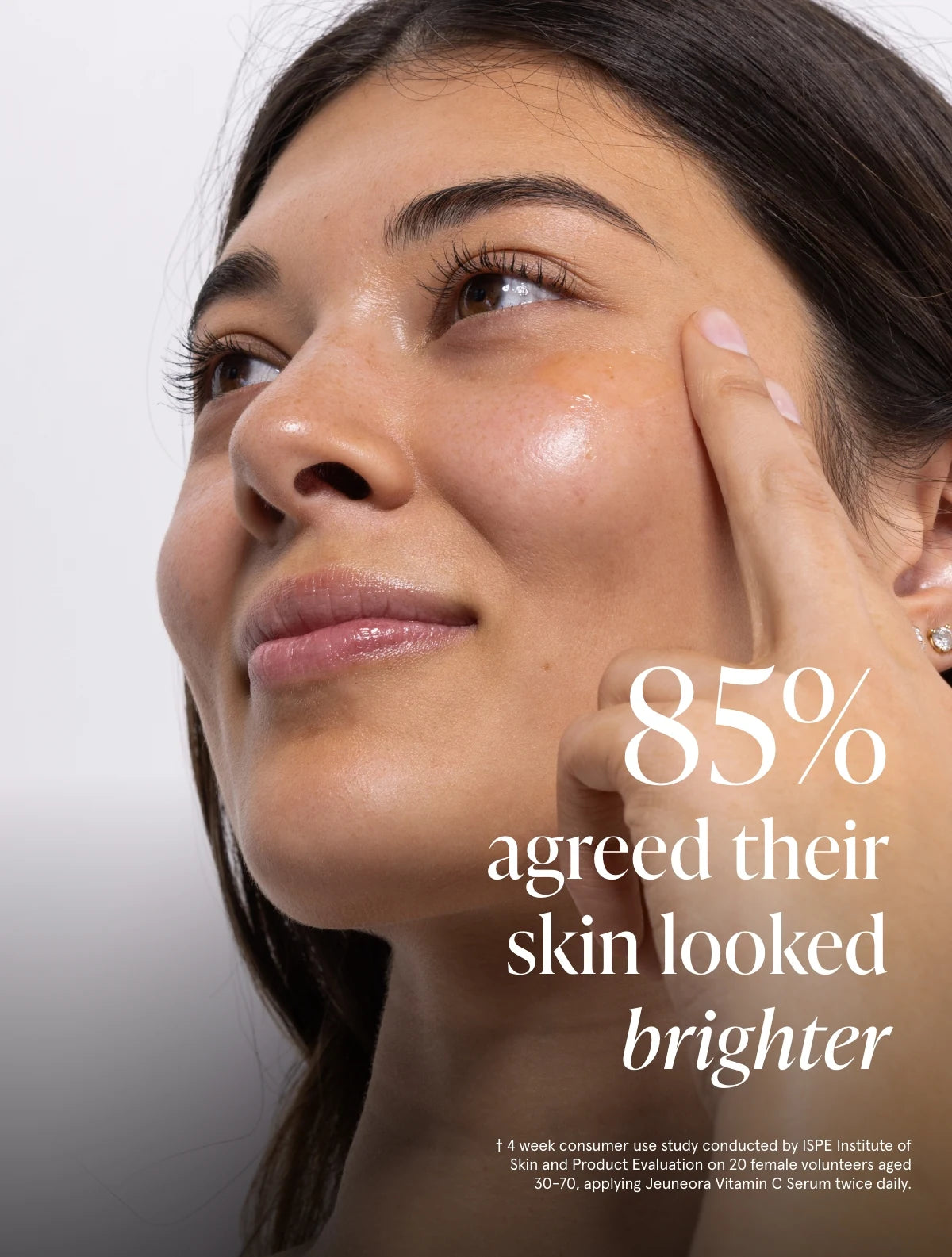 Close-up of a woman touching her cheek with text overlay reading '85% agreed their skin looked brighter' on a light gray background.