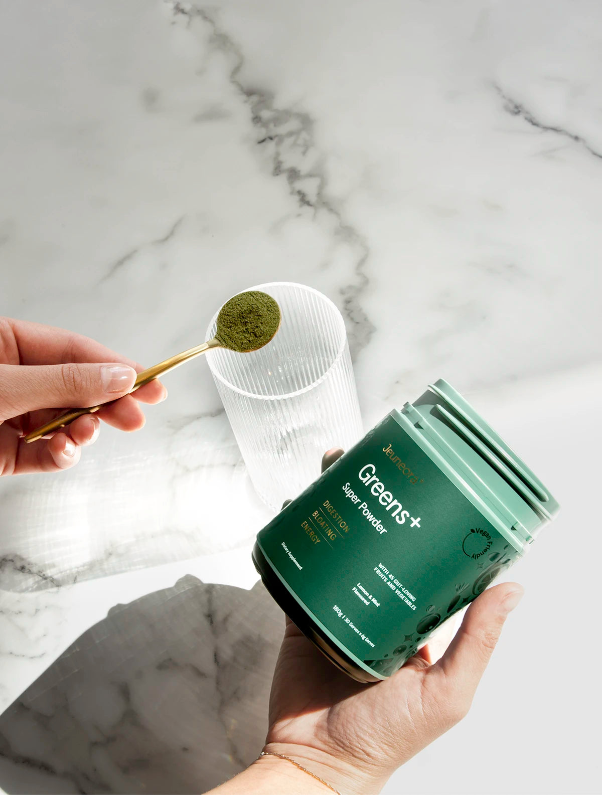 Greens+ Super Powder supplement being placed into glass 