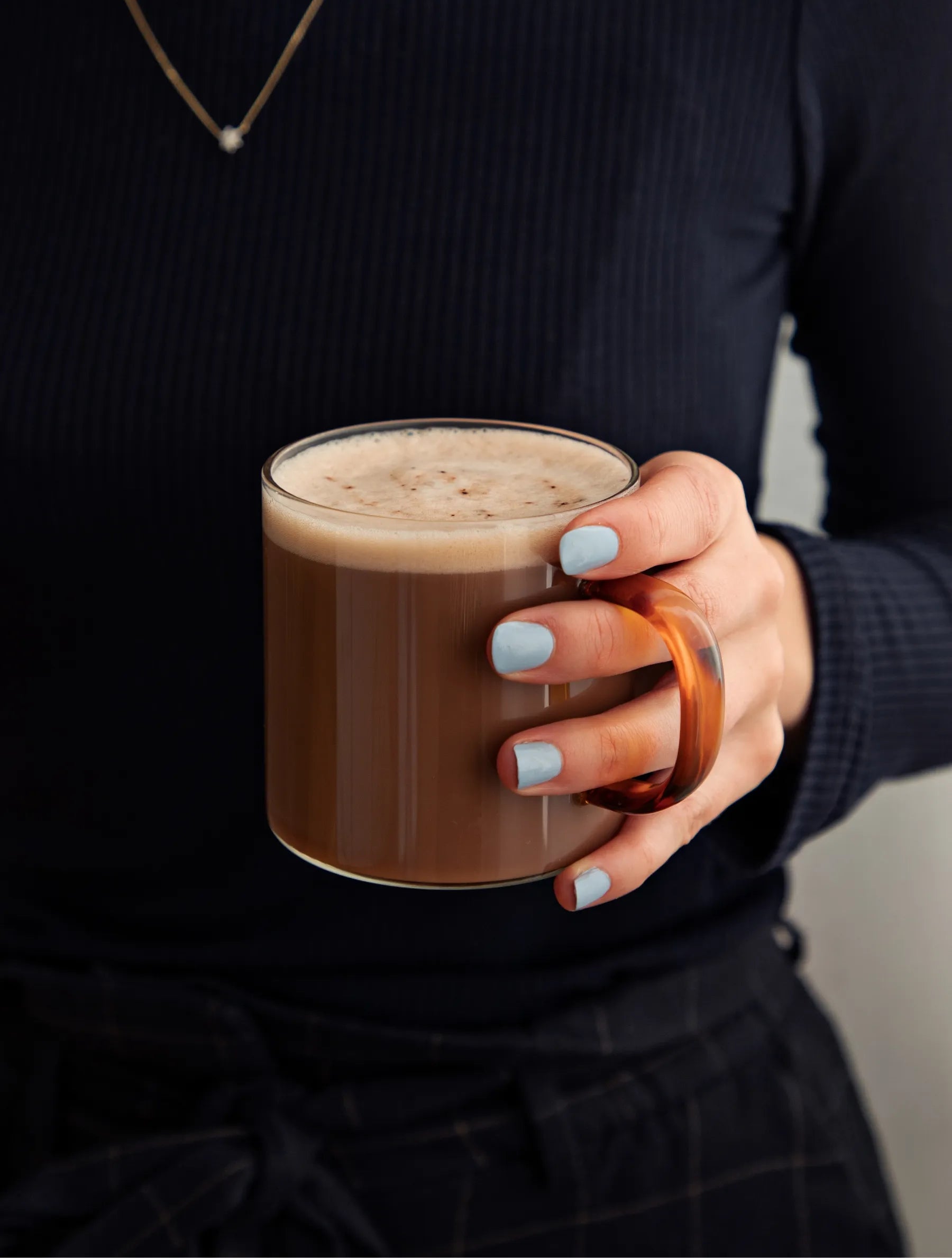 Woman with bright blue nail polish holding a mug of Jeuneora Beauty Sleep hot chocolate.